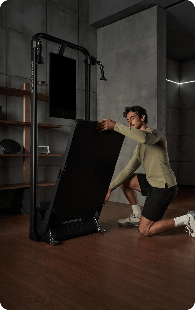 Person setting up a black exercise machine in a room with a television on the wall.