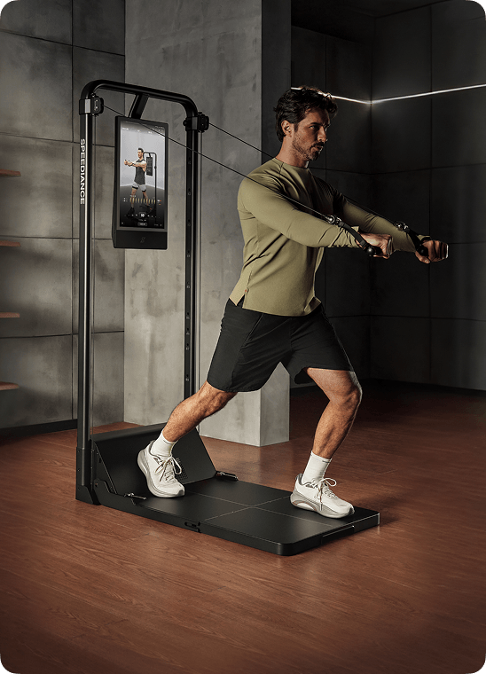Man exercising on a fitness machine with a screen displaying workout instructions in a dimly lit room.