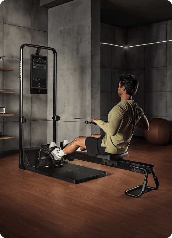 Person using a home gym machine in a room with concrete walls and wooden floor.