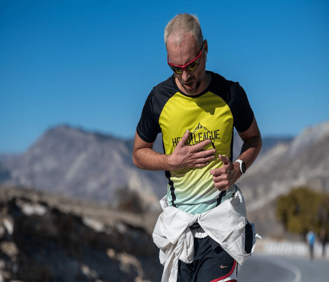 A male runner running outdoors with mountains and a blue sky in the background.