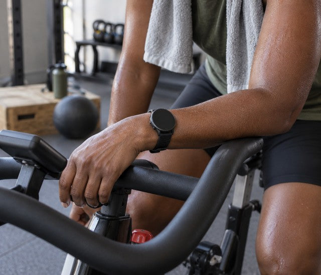 Fitness watch on an athlete's wrist resting on an indoor bike handlebar