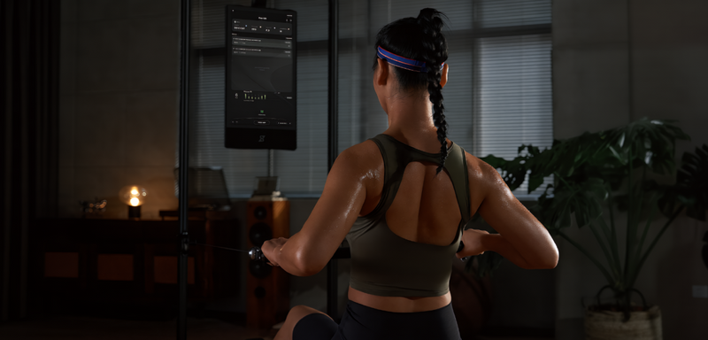 Woman exercising in a dimly lit room with a television screen displaying workout information.