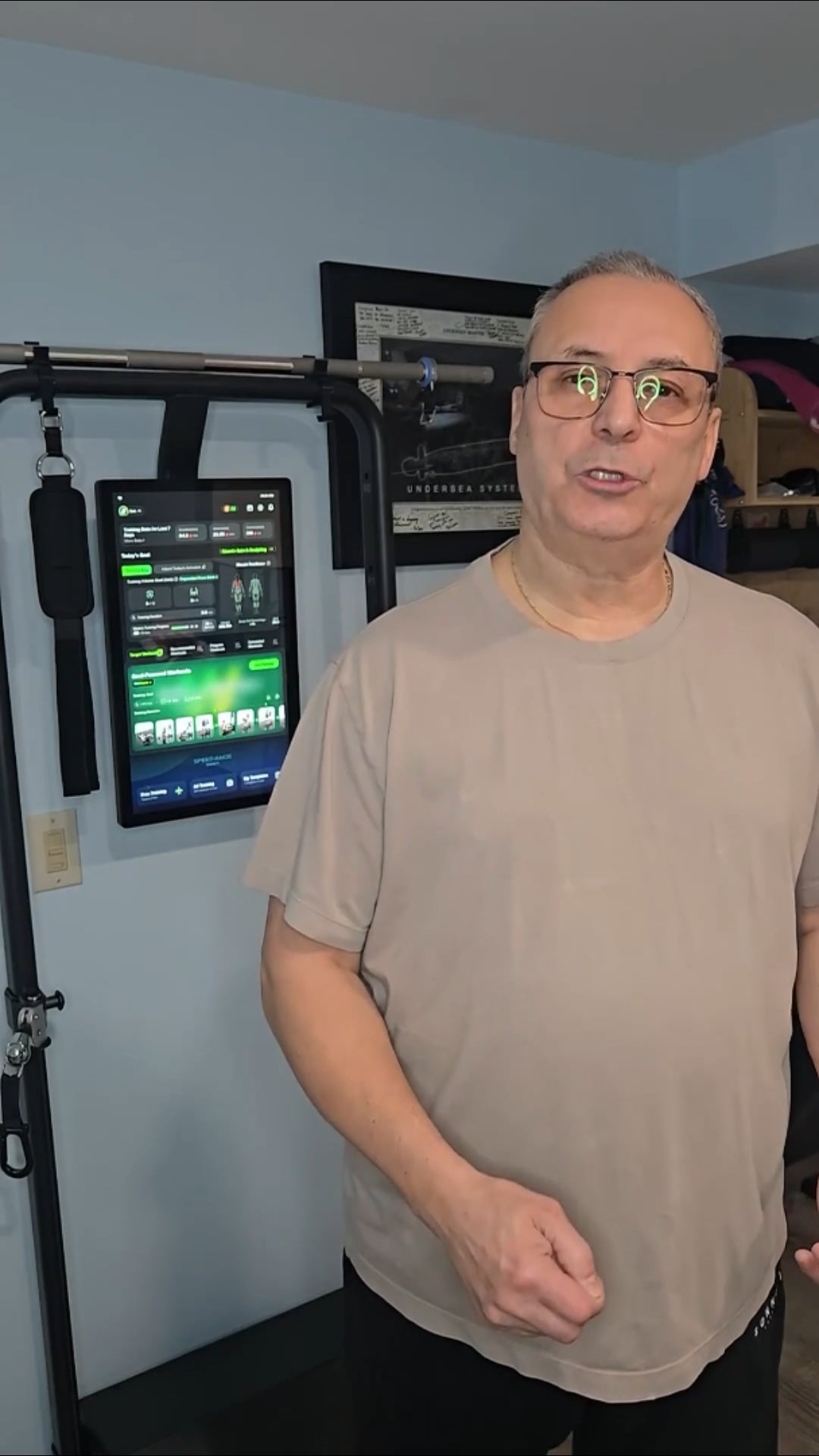 Man standing in a room with exercise equipment and a screen displaying workout information.