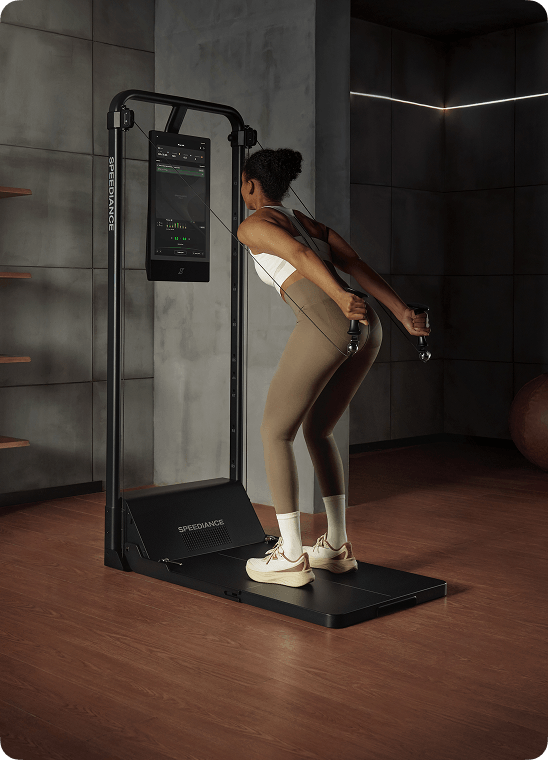 Person using a black fitness machine with a digital display in a dimly lit room.